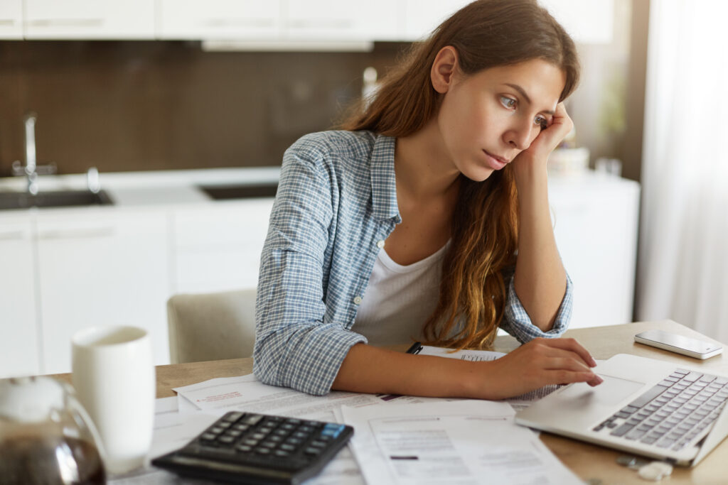 Picture Of Thoughtful Focused Young Housewife Studying Loan Agreement, Searching For Information On Internet Using Laptop Computer. Attractive Female Working Through Finances At Kitchen Table - PAVON | Contabilidade em São Paulo