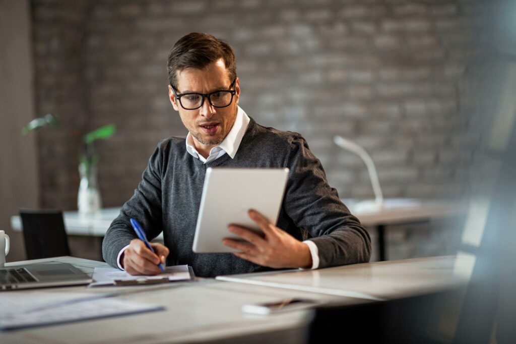 Male Entrepreneur Writing Business Report While Using Digital Tablet Office - PAVON | Contabilidade em São Paulo