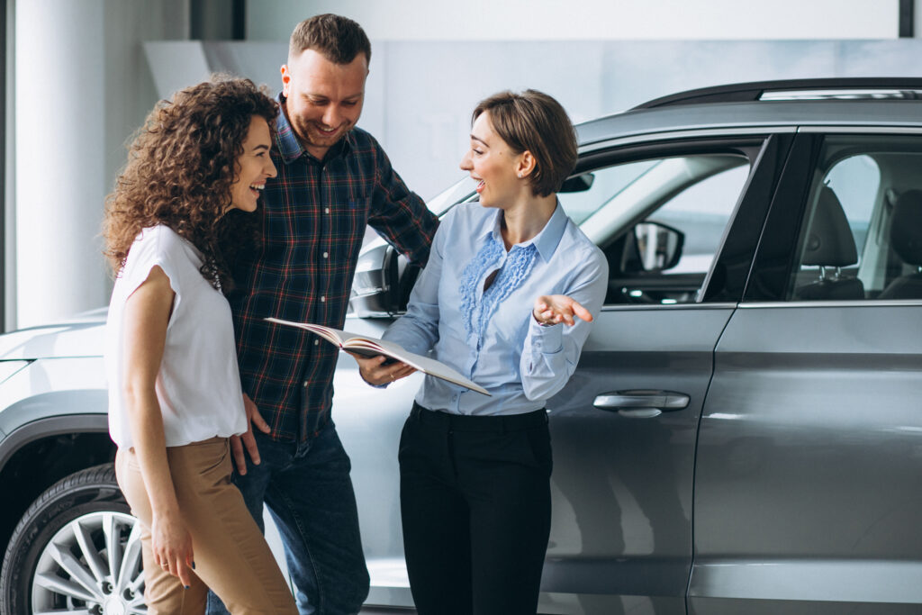 Young Couple Talking To A Sales Person In A Car Showroom - PAVON | Contabilidade em São Paulo