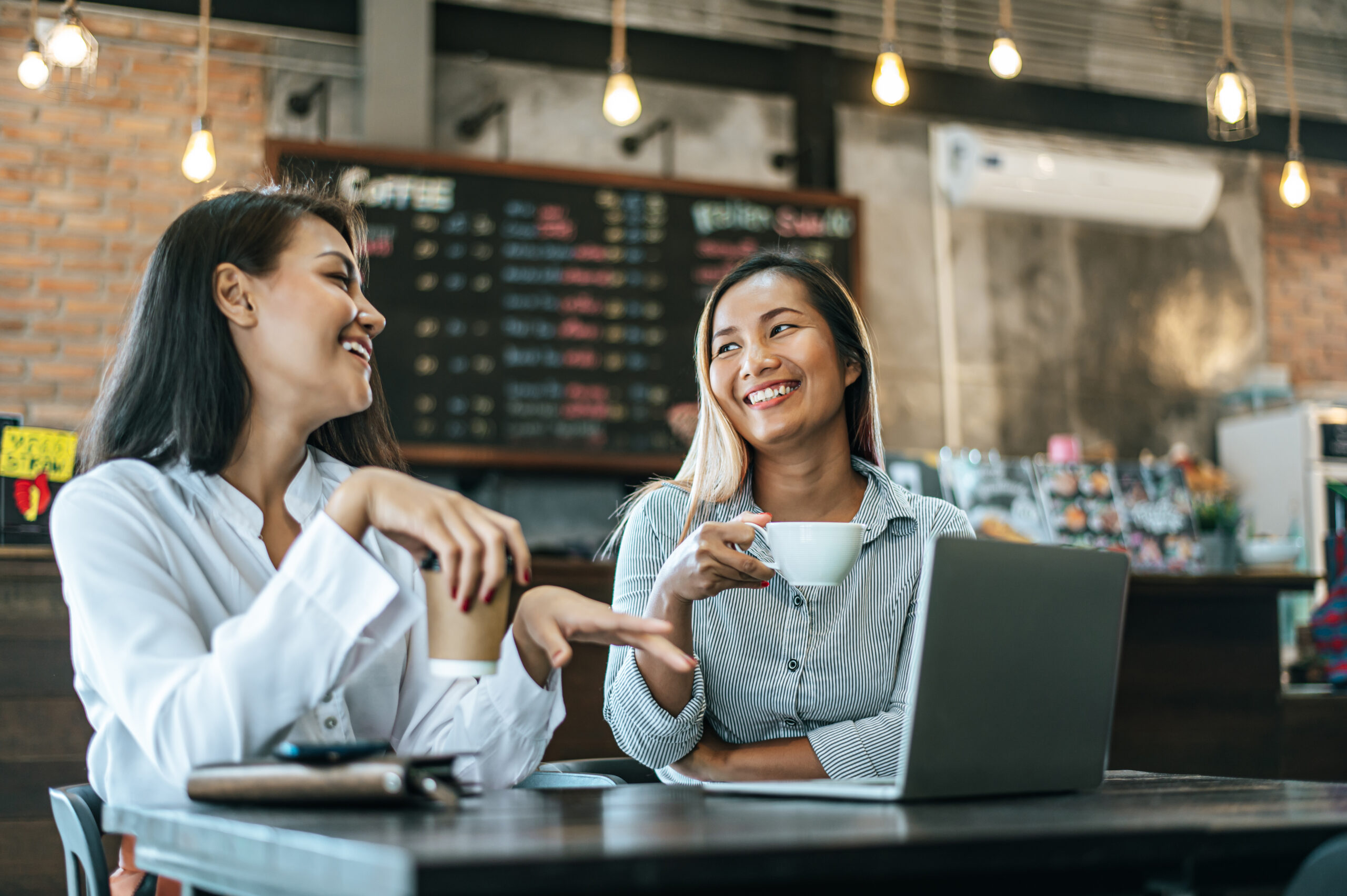 Two Women Sitting And Working With A Laptop In A Coffee Shop - PAVON | Contabilidade em São Paulo