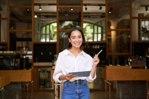 Portrait Of Asian Woman, Manager Standing With Tablet In Front Of Cafe Entrance, Welcomes Guests - PAVON | Contabilidade em São Paulo